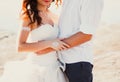 Wedding couple hugs on the sea beach. Sunny summer photo. Bride with hair down in off shoulder dress with train. Ocean romantic