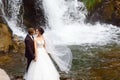 Wedding, couple kiss in hills near beautiful grand waterfall in mountain. Wind fluttering a long veil. Landscape of hills and moun Royalty Free Stock Photo