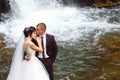 Wedding couple kissing and hugging on rocks near beautiful grand waterfall in mountain Royalty Free Stock Photo