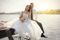 Wedding couple sitting on bridge near lake on sunset at wedding day. Bride and groom in love Royalty Free Stock Photo