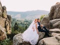 Wedding couple sitting at rocky mountains against the sky. Cute romantic moment. Royalty Free Stock Photo