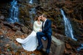 Wedding couple sitting on the stone and posing. Waterfall in mountains background. Fall Royalty Free Stock Photo