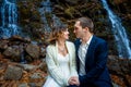 Wedding couple sitting on the stone. Waterfall background. Honeymoon in autumn mountains Royalty Free Stock Photo