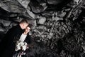 Destination Iceland wedding. Wedding couple under a rock of basalt stones. Bride and groom on the black beach of Vik. Royalty Free Stock Photo