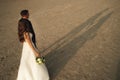 Wedding couple walking on sandy beach. Bride and groom casting long shadow in evening sun. Wedding day concept. Royalty Free Stock Photo