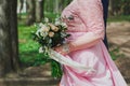 Wedding couple walks in green summer park. Groom`s hands on bride`s waist. Curvy woman in pink lace evening dress. Wedding bouqu Royalty Free Stock Photo