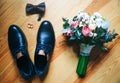 Wedding day accessories. Groom`s shoes with bouquet on the wooden background. Golden rings and bow tie are nearby. Stylish things Royalty Free Stock Photo