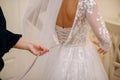 On the wedding day, the bride wears a white wedding dress. A faithful friend helps to tie ribbons on a corset, back view Royalty Free Stock Photo