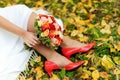 Wedding day. Close up of bride`s feet in red shoes, colorful bridal bouquet and autumn leaves on green grass Royalty Free Stock Photo