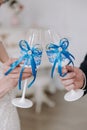 Wedding day. Hands of the bride and groom are holding wedding glasses with champagne, decorated in blue. Blue bow on glasses. Royalty Free Stock Photo