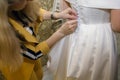 On the wedding day, the mother of the bride helps her daughter put on the wedding dress and button up the buttons