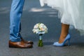 Wedding details: classic brown and blue shoes of bride and groom. Bouquet of roses standing on the ground between them. Newlyweds