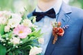 Wedding details close up. Groom in blue suit wearing boutonniere with red flowers and holding bridal bouquet Royalty Free Stock Photo