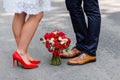 Wedding details: stylish red and brown shoes of bride and groom. Bouquet of roses standing on the ground between them. Newlyweds s Royalty Free Stock Photo