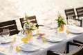 Wedding dinner table reception. Rectangular tables with white tablecloth, floral arrangements lemons in vases. Yellow