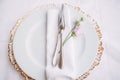 Wedding dinner table reception. White plate on top of a wildcard with golden edges. In a white plate there is a napkin