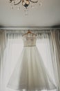 Wedding dress. White wedding dress with a full skirt on a hanger in the room of the bride with white curtains. Wedding