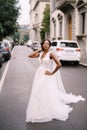 Wedding in Florence, Italy. African-American bride in a white dress, with a long veil, walks along the road on a city