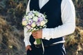 Wedding. The groom in a white shirt and waistcoat are holding bouquets of of white roses, hypericum, lisianthus, chrysanthemum,