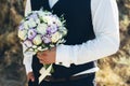 Wedding. The groom in a white shirt and waistcoat are holding bouquets of of white roses, hypericum, lisianthus, chrysanthemum,