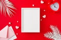 Flat lay photo of white tropical leaves, hearts, envelope, alarm clock on red background