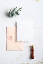 Wedding invitation card mockup, envelope, wax seal stamp, eucalyptus branch on marble table. Wedding stationery set. Flat lay, top