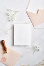 Wedding invitation card mockup, pink envelopes, wax seal stamp, gypsophila branches on marble desk. Elegant wedding stationery set