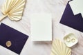 Wedding invitation card mockup, purple envelopes, golden rings, dried flowers on marble desk. Elegant wedding stationery set. Flat