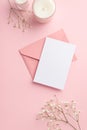 Wedding invitation concept. Top view vertical photo of pink envelope postcard candles and white gypsophila flowers on isolated