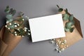 Wedding invitation or greeting card mockup with envelope and eucalyptus twigs and gypsophila flowers.