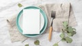 Wedding menu card on plate with fork on linen napkin on marble table with green leaves