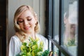 Wedding morning of the bride. Exquisite blonde in a delicate peignoir standing near the window with a bouquet of flowers in her Royalty Free Stock Photo