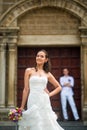 Wedding photo with bride and groom. Beautiful bride posing, and behind her is the groom near the Catholic Church Royalty Free Stock Photo