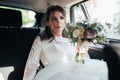 Wedding photo of the bride who is sitting in the car with a bouquet of flowers Royalty Free Stock Photo