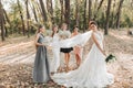Wedding photo in nature. The bridesmaids stand behind the bride, holding their bouquets and her veil, the bride holds the bouquet Royalty Free Stock Photo