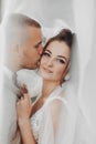 Wedding portrait of the bride and groom. Happy bride and groom gently hug each other under the veil, pose and kiss. Royalty Free Stock Photo