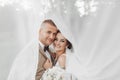 Wedding portrait of the bride and groom. Happy bride and groom gently hug each other under the veil, pose and kiss. Royalty Free Stock Photo