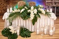 Wedding presidium in restaurant, copy space. Banquet table for newlyweds with monstera palm leaves, orchid flowers and candles.