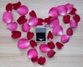 Wedding ring with pink and red rose petals in heart shape on wooden surface Royalty Free Stock Photo
