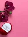 Wedding ring in a red box and red orchid on pink background. Valentine's Day. Royalty Free Stock Photo