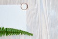 Wedding ring with a sheet of white paper and a green branch on a wooden background. Top view Royalty Free Stock Photo