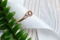 Wedding ring in a white ribbon and a green branch on a wooden background. Top view Royalty Free Stock Photo