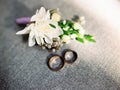 Wedding rings with groom`s boutonniere, white, purple and green floral decorations on grey background. Wedding blog concept Royalty Free Stock Photo