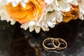 Wedding rings lie on a bouquet of orange roses and white colors. Royalty Free Stock Photo