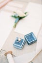 Wedding rings lie in a box on the table near the invitations and a white ribbon on a reel