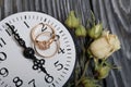 Wedding rings lie on the dial of the watch. Nearby dried roses. On brushed pine boards painted in black and white Royalty Free Stock Photo