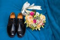 Wedding rings lie on men`s shoes, next to a beautiful wedding bouquet on a blue background Royalty Free Stock Photo