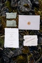 Wedding rings lie on moss-covered stones, surrounded by decorated invitations and envelope sealed with sealing wax