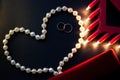 Wedding rings, a string of pearls on a black background, burning lights, a red box. St. Valentine`s Day Royalty Free Stock Photo