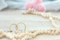 wedding rings on wooden white table, pearls beads, pink rose bouquet, selective focus Royalty Free Stock Photo